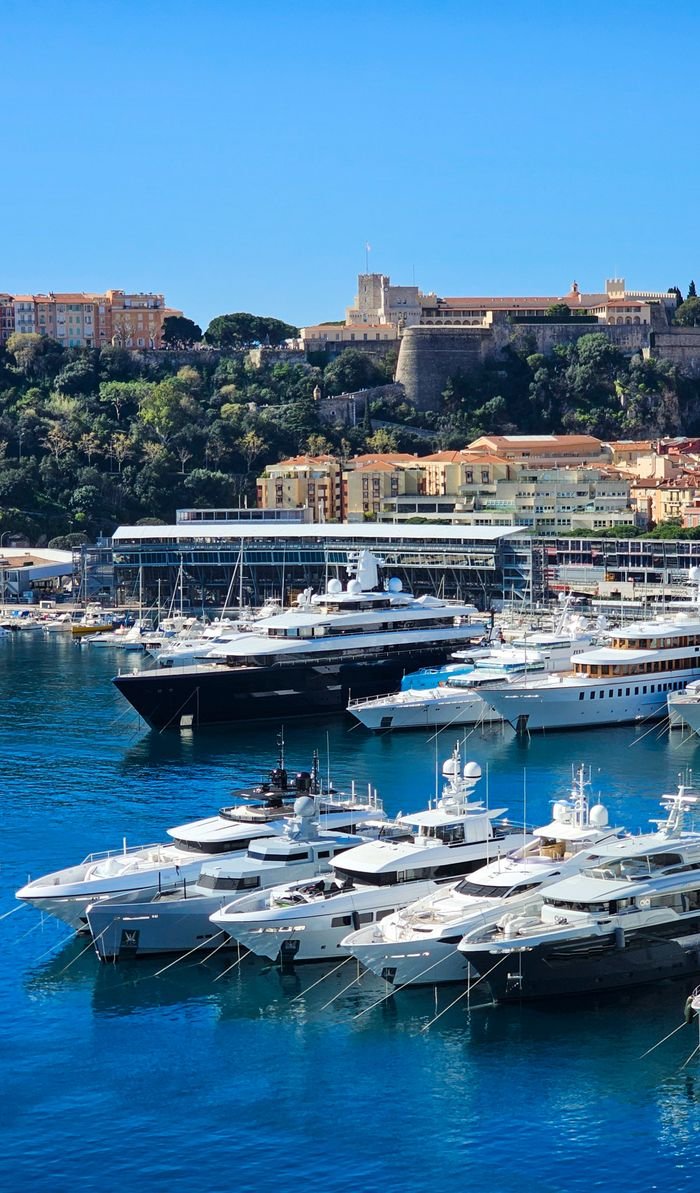 Scenic view of luxury yachts docked in Monaco harbor with the historic cityscape in the background.