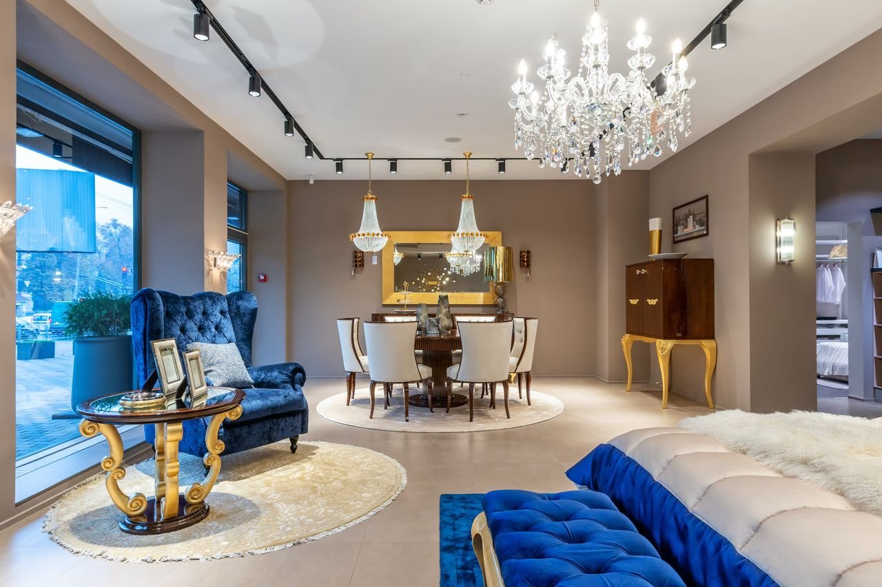 Round table with chairs placed neat armchair in spacious room with vintage cabinet and comfortable bed in apartment with window